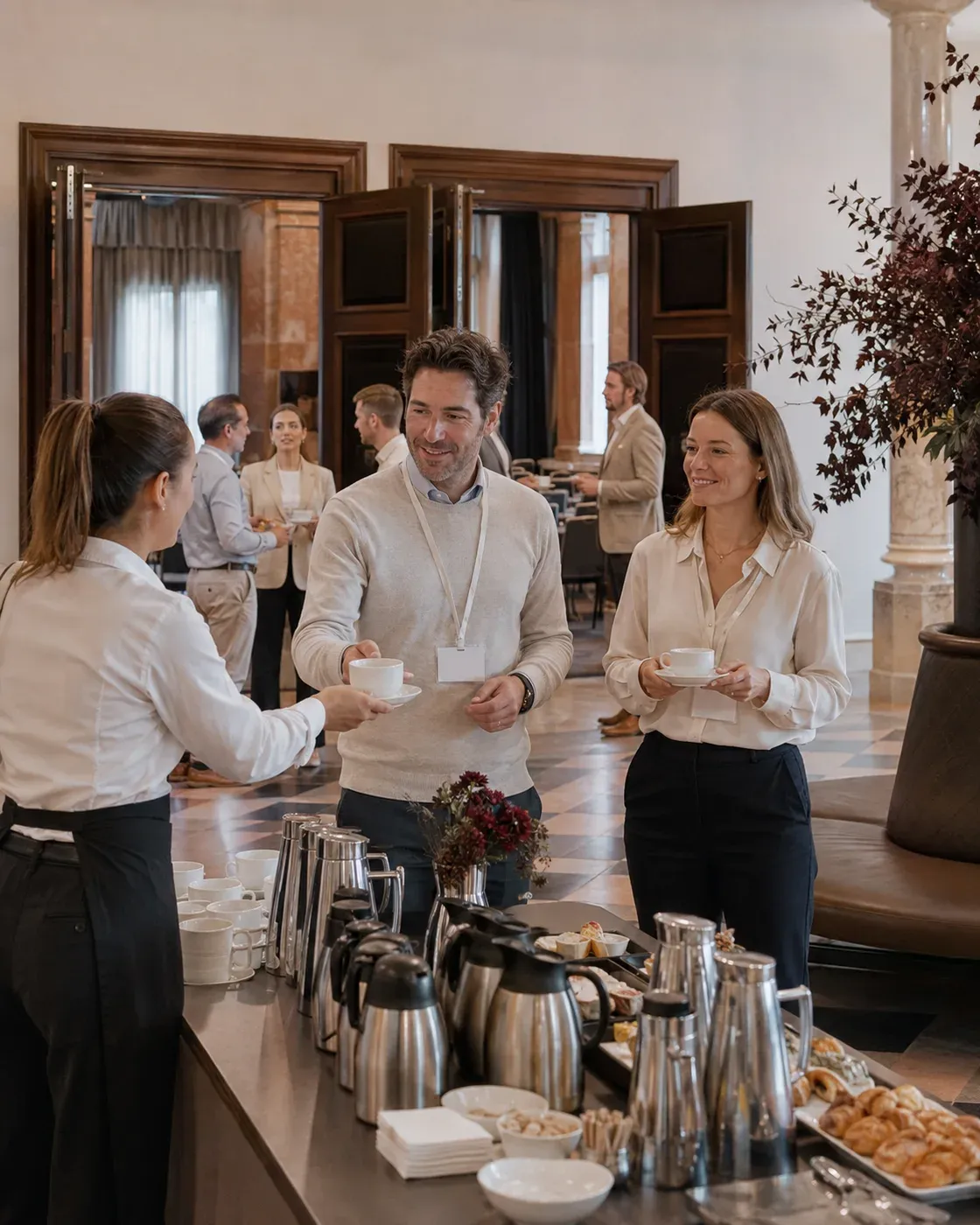 Illustrative scene of conference guests wearing badges receiving drinks from a team member between two meeting rooms.