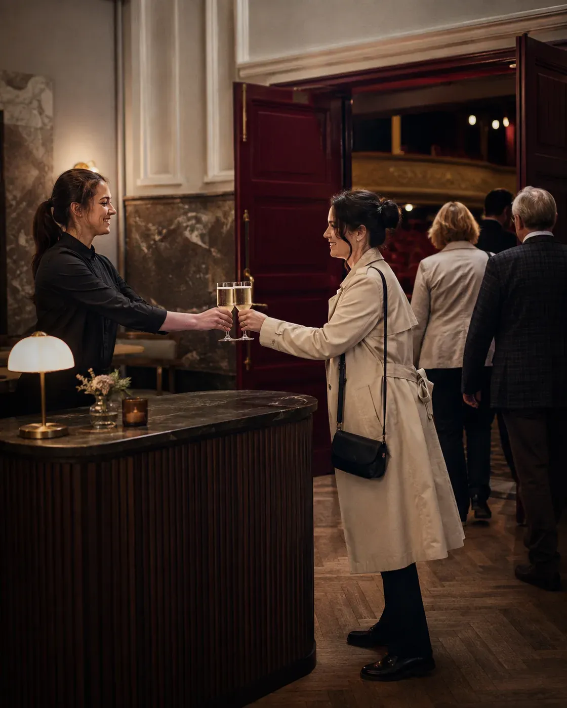 Illustrative scene of a team member handing prepared drinks to guests at a foyer counter, with the auditorium doors behind them.