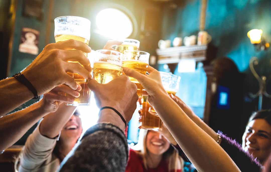 Eine Gruppe Gäste stößt in einer vollen Bar mit Bier an.